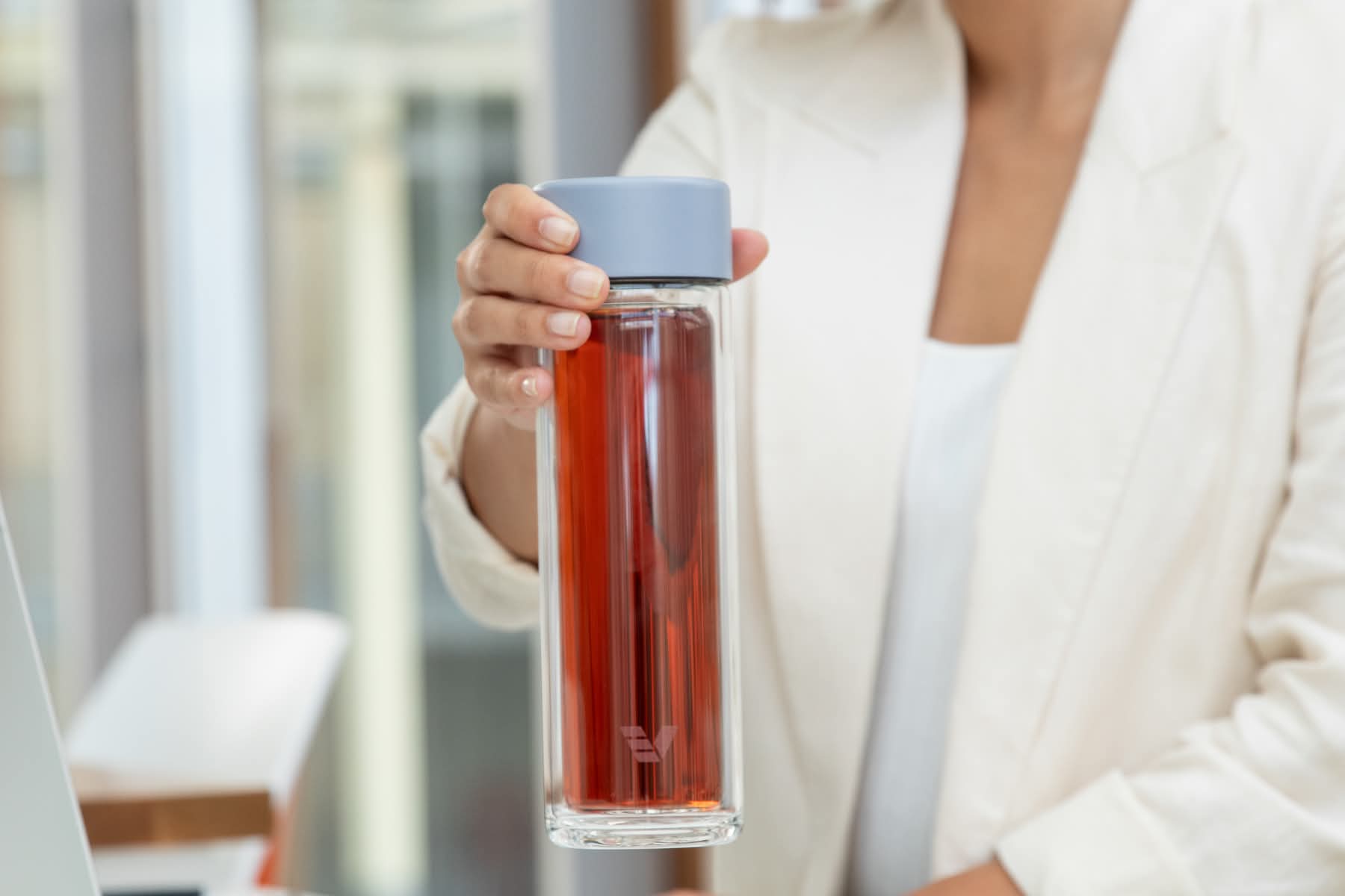 Female lifting an Ever Vessel Glass Multi double wall glass tea flask bottle with lilac colored lid and black infused tea inside at her desk.