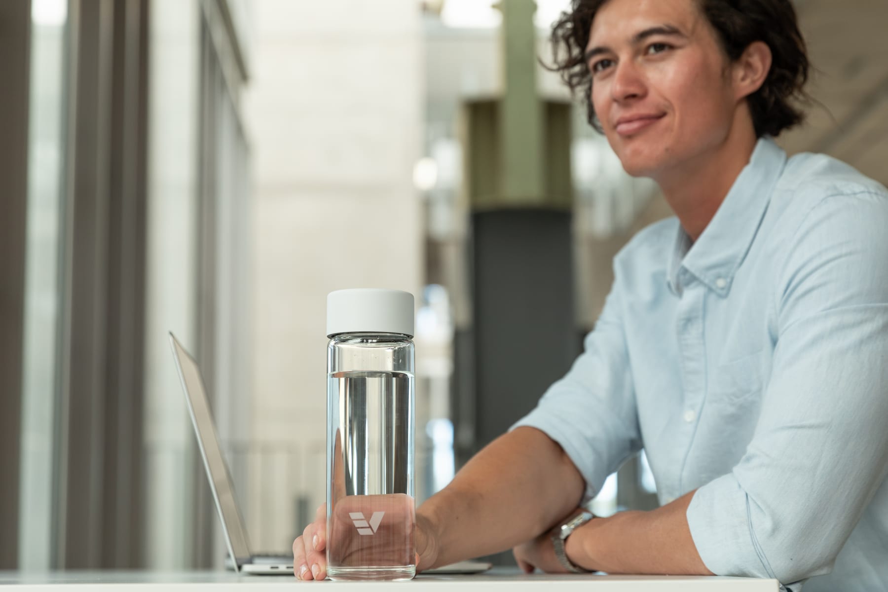 A male picking up his Ever Vessel Glass water bottle with a white lid off his desk.