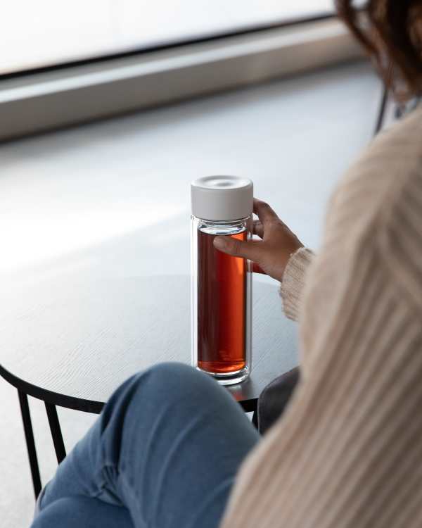 Female holding an Ever Vessel Glass Multi double walled glass tea flask bottle with white colored lid and black infused tea inside.