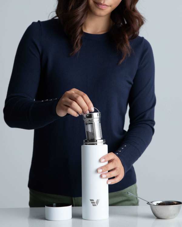 A female inserting the tea infuser into her Ever Vessel Multi white stainless steel tea infuser water bottle at the kitchen bench.