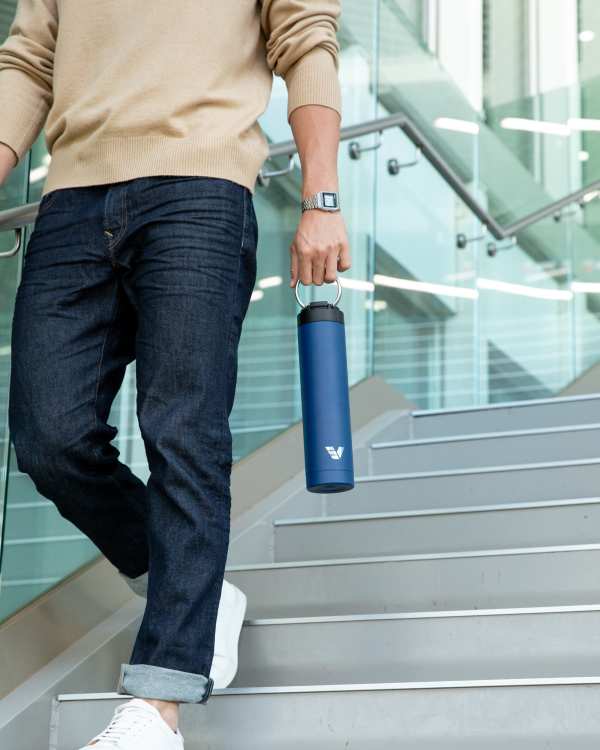 A male holding an Ever Vessel Super Maxi Blue stainless steel water bottle by the integrated carry handle down the stairs at work.