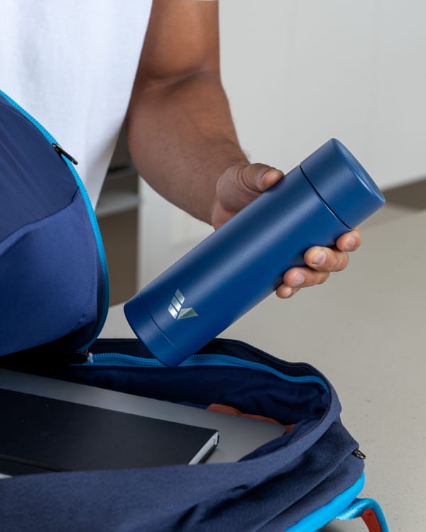 A male packing his Ever Vessel Multi Blue stainless steel tea infuser water bottle into his backpack.