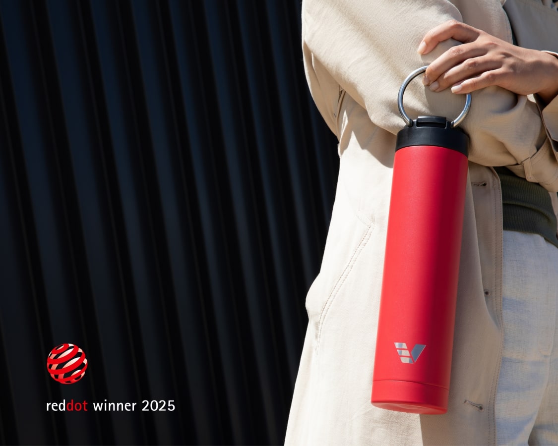 A female holding her Ever Vessel Super Maxi Red water bottle by the integrated handle  with the Red Dot Design Award logo.
