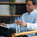 A male sitting in chair holding his Ever Vessel Glass Multi glass double wall tea infuser water bottle with blue lid at the cafe.