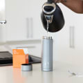 A male pouring hot water into his Ever Vessel Multi stainless steel tea infuser water bottle on the kitchen bench.