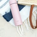 A Personalized Ever Vessel Multi Rose pink stainless steel tea infuser water bottle on a beach towel with the engraved name LANA on the side