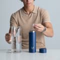 A male putting ice into his Ever Vessel Multi Blue stainless steel tea infuser water bottle on the kitchen bench.