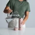 A female filling her Ever Vessel Multi Rose Pink stainless steel tea infuser water bottle with iced water at the kitchen bench.