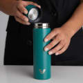 Female taking the lid off her Ever Vessel Mini Teal green small water bottle at a stone bench.