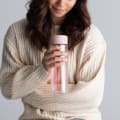 Female holding a Ever Vessel Glass Multi double walled glass tea infuser bottle with the rose pink lid and berry infused tea inside.