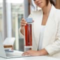Female lifting an Ever Vessel Glass Multi double wall glass tea flask bottle with lilac colored lid and black infused tea inside at her desk.