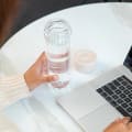 A female about to drink from her Ever Vessel Glass Multi double walled glass tea infuser bottle with the desert beige lid removed at her desk.