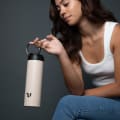 A female holding her Ever Vessel Maxi Desert beige stainless steel water bottle by the integrated carry handle.