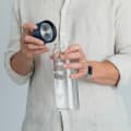 A male about to drink from his Ever Vessel Glass water bottle with blue lid removed at home.