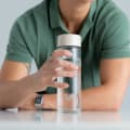 A male holding his Ever Vessel Glass water bottle with desert beige lid on a kitchen bench.