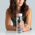 A female holding her Ever Vessel Glass water bottle with rose pink lid on a kitchen bench.