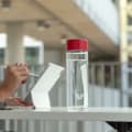 An Ever Vessel Glass water bottle with red lid on an open plan work desk next to a person working at his laptop.