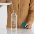 A male filling his Ever Vessel Glass water bottle with teal green lid at the kitchen bench.