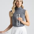 A female holding her Ever Vessel Glass water bottle with stainless lid above a stone table at work.