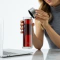 A female taking off the stainless grey lid from her Ever Vessel Glass Multi double walled glass tea infuser water bottle at her desk.