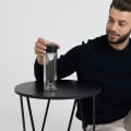 A male picking up his Ever Vessel Glass Multi double walled glass tea infuser water bottle with a black lid off a small side table.