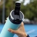 A female about to drink from her Ever Vessel Maxi Mint Green stainless steel water bottle with the leak-proof flip top open on the tennis court.