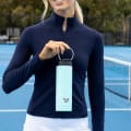 Female holding her Ever Vessel Maxi Mint Green stainless steel water bottle by the integrated handle at the tennis court.