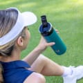 Female about to drink from her Ever Vessel Maxi Teal Green stainless steel water bottle with leak-proof flip top open on the golf course.