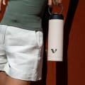 Female holding her Ever Vessel Maxi Desert Beige stainless steel water bottle by the integrated carry handle.