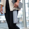A female carrying her Ever Vessel Maxi Lilac stainless steel water bottle by the integrated carry handle on the way to the office.