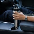 A male placing an Ever Vessel Super Maxi stainless steel water bottle into a car cup holder with the leak-proof flip top open.