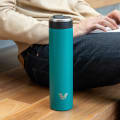 An Ever Vessel Super Maxi Teal stainless steel water bottle on a polished wooden bench next to a male working on his laptop at the office cafeteria.