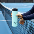 Female holding her Ever Vessel Maxi Mint Green stainless steel water bottle over the tennis court net.