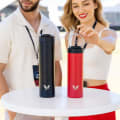 Female and Male attending an event with their Ever Vessel Super Maxi Black and Maxi Red stainless steel water bottles sitting on a round bar table.