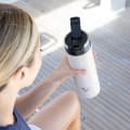 A female about to drink from her Ever Vessel Maxi Desert Beige stainless steel water bottle on a yacht with the leak-proof flip top open.