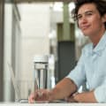 A male picking up his Ever Vessel Glass water bottle with a white lid off his desk.