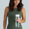 A female holding her Ever Vessel Glass water bottle with white lid at home.