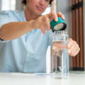 A male taking off the teal green lid from his Ever Vessel Glass water bottle at his desk.
