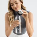 Female holding her optically clear borosilicate glass water bottle, with white lid off at the office.