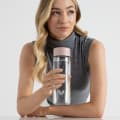 A female holding her Ever Vessel Glass water bottle with rose pink lid above a stone bench at work.