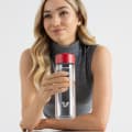A female holding her Ever Vessel Glass water bottle with red lid above a stone bench at work.