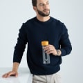 A male holding his Ever Vessel Glass water bottle with yellow lid next to a stone bench.