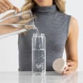 A female filling her Ever Vessel Glass water bottle with Desert beige lid at the office.