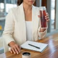 A female drinking tea from her Ever Vessel Glass Multi double walled glass tea infuser water bottle with Desert beige lid at her work desk.