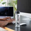 A male at his desk next to his  Ever Vessel Glass Multi glass double wall tea infuser water bottle with black lid.