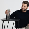 An Ever Vessel Glass Multi  double walled glass tea infuser water bottle with stainless grey lid sitting on a small table next to a seated male.