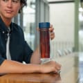 Male holding an Ever Vessel Glass Multi Blue double wall glass tea infuser water bottle with blue lid and tea inside at his desk.
