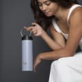 A female holding her Ever Vessel Maxi Lilac stainless steel water bottle by the integrated carry handle in a studio.
