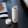 An Ever Vessel Multi Desert beige stainless steel tea infuser water bottle with the Straw Attachment accessory sitting on a desk.
