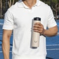 A male holding his Ever Vessel Super Maxi Desert Beige stainless steel water bottle on a tennis court.